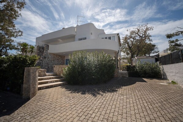 A modern two-story house with a stone facade, a curved balcony, and a paved driveway.