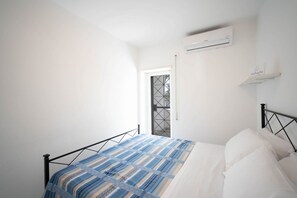 A bedroom with a bed, a window, an air conditioning unit, and a door.