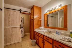 A bathroom with wooden cabinets, a sink, a mirror, and a washing machine. - Views of Elk River with wrap-around screened porch for family time (Athens)