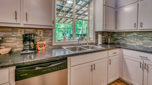 A kitchen with white cabinets, a coffee maker, a bag of Dunkin' Donuts, a dishwasher, and a window with a view of trees. - Views of Elk River with wrap-around screened porch for family time (Athens)