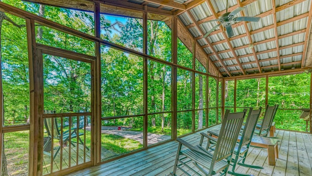 A covered wooden deck with large windows, wooden chairs, and a ceiling fan. - Views of Elk River with wrap-around screened porch for family time (Athens)