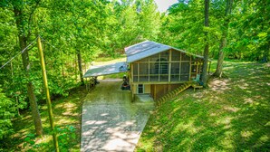 A wooden cabin with a covered porch, surrounded by dense forest. - Views of Elk River with wrap-around screened porch for family time (Athens)