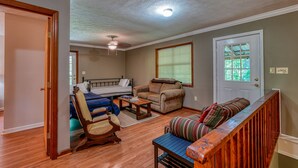 A cozy living room with a bed, a rocking chair, a sofa, and a wooden staircase. - Views of Elk River with wrap-around screened porch for family time (Athens)