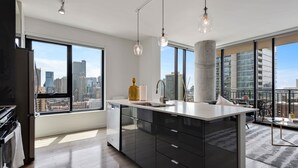 Eine moderne Küche mit einer großen Kochinsel, einem Geschirrspüler und einer Spüle. Große Fenster bieten Blick auf die Stadt.