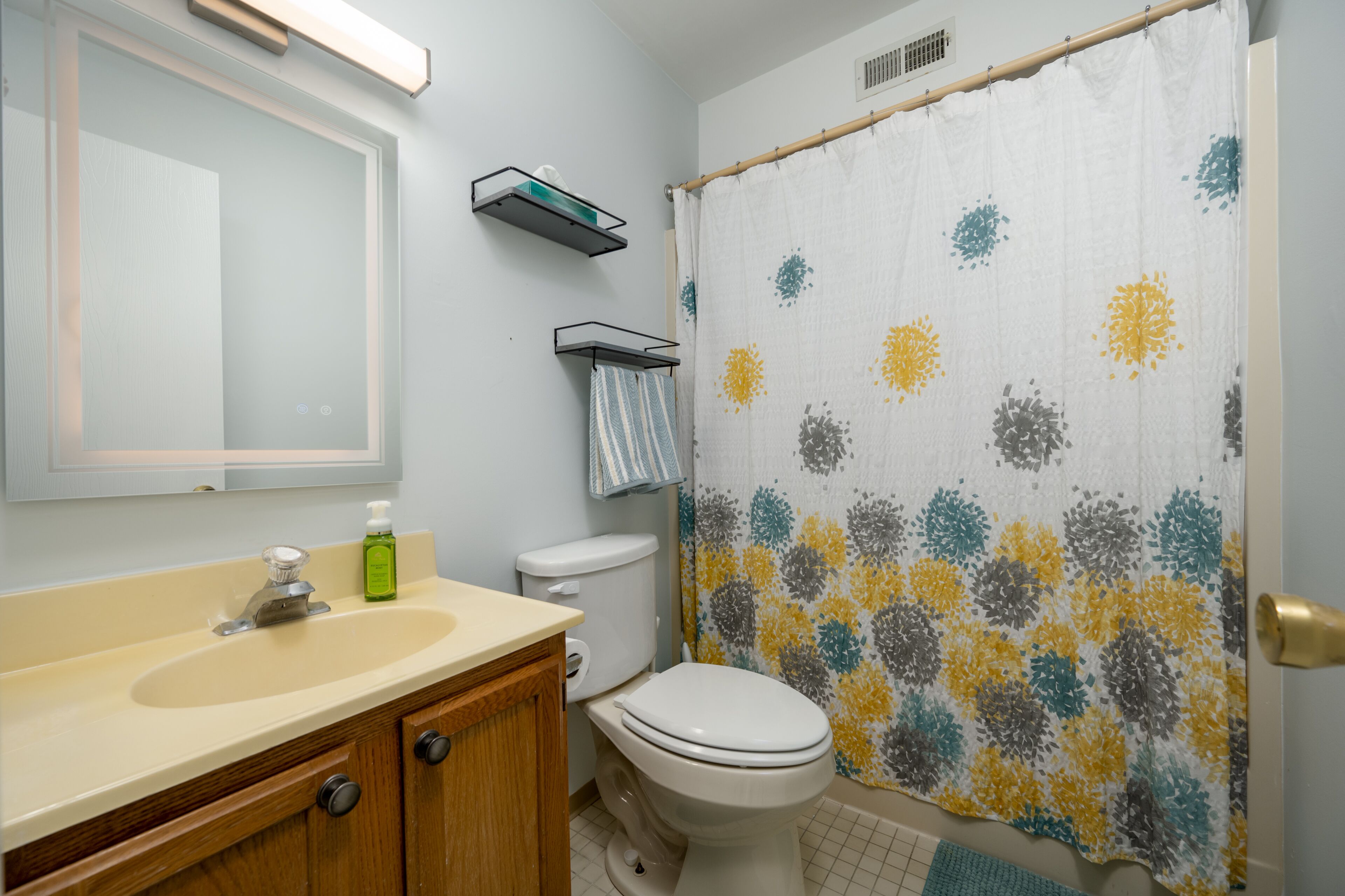 A bathroom with a sink, mirror, toilet, and shower curtain.
