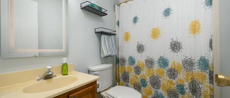 A bathroom with a sink, mirror, toilet, and shower curtain.
