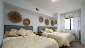 A hotel room with two beds, each with patterned bedding and pillows, a large mirror, and woven wall art. - Contemporary, clean 1-bedroom mid-town condo with bay view and 1 block to beach. (Ocean City)