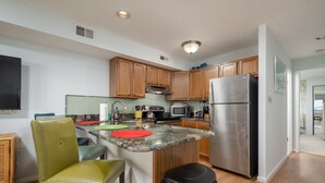 A modern kitchen with wooden cabinets, a stainless steel refrigerator, and a granite countertop. - Contemporary, clean 1-bedroom mid-town condo with bay view and 1 block to beach. (Ocean City)