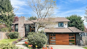 A modern two-story house with a brick exterior, a large garage, and a well-maintained garden with colorful flowers. - Beautifully renovated hot-tub, large fenced backyard, pet friendly (Kirkland)