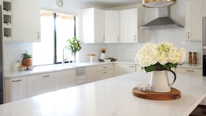 A modern kitchen with white cabinets, a marble countertop, a clock, and a vase of flowers. - Beautifully renovated hot-tub, large fenced backyard, pet friendly (Kirkland)