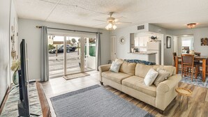 A living room with a beige sofa, a flat-screen TV, and a ceiling fan. - Oceanside Ormond Beach Condo, Steps to Shore! (Ormond Beach)