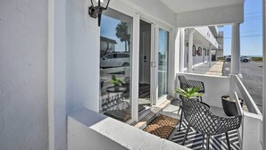 A balcony with a glass door, two chairs, and a potted plant. - Oceanside Ormond Beach Condo, Steps to Shore! (Ormond Beach)