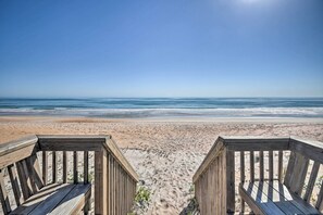 En træterrasse der fører ned til en strand med kig til havet.