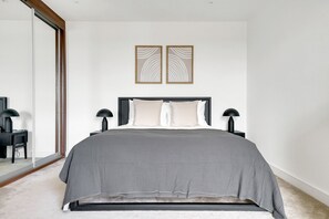 Un dormitorio moderno con una cama grande, dos lámparas de noche y un ventanal de vidrio que da a un balcón.