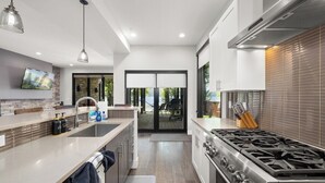 A modern kitchen with a central island, stainless steel appliances, and a large window. - Monthly 3BR Condo Rental on Whitefish Lake (Whitefish)