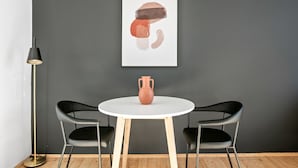 Ein modernes Zimmer mit einem runden weißen Tisch, zwei schwarzen Stühlen, einer einzelnen Vase und einer Stehlampe.