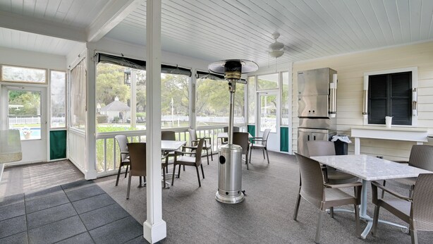 Uma área de varanda coberta com mesa, cadeiras e ventilador de teto, com vista para os arredores.