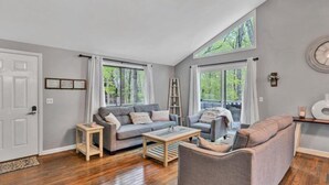 A spacious living room with a grey sofa set, a coffee table, and a view of the outdoors through large windows. - Hokie Hideaway- Pet-friendly home with a fire-pit to enjoy with the family. (Huddleston)