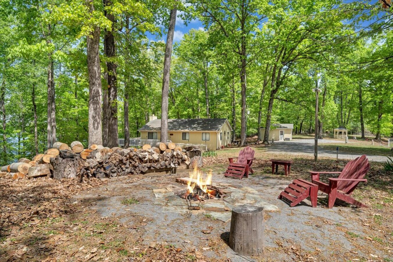 A campsite with a fire pit, wooden chairs, and a pile of logs.