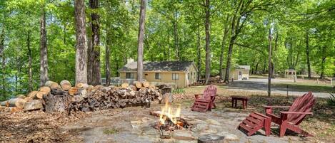 A campsite with a fire pit, wooden chairs, and a pile of logs.