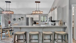 A modern kitchen with a large island, bar stools, pendant lights, and white cabinetry. - Hokie Hideaway- Pet-friendly home with a fire-pit to enjoy with the family. (Huddleston)