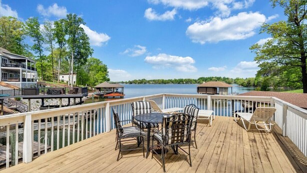 A wooden deck with outdoor furniture, a view of a lake, and a dock with a boat. - Hokie Hideaway- Pet-friendly home with a fire-pit to enjoy with the family. (Huddleston)