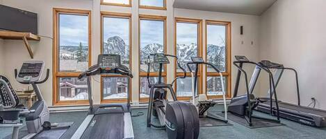 Une salle de sport équipée de tapis de course, d’appareils elliptiques et d’un vélo d’appartement, avec de grandes fenêtres offrant une vue sur les montagnes.
