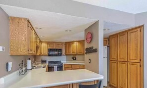 A kitchen with wooden cabinets, a central island with two chairs, a microwave, stove, and a refrigerator.