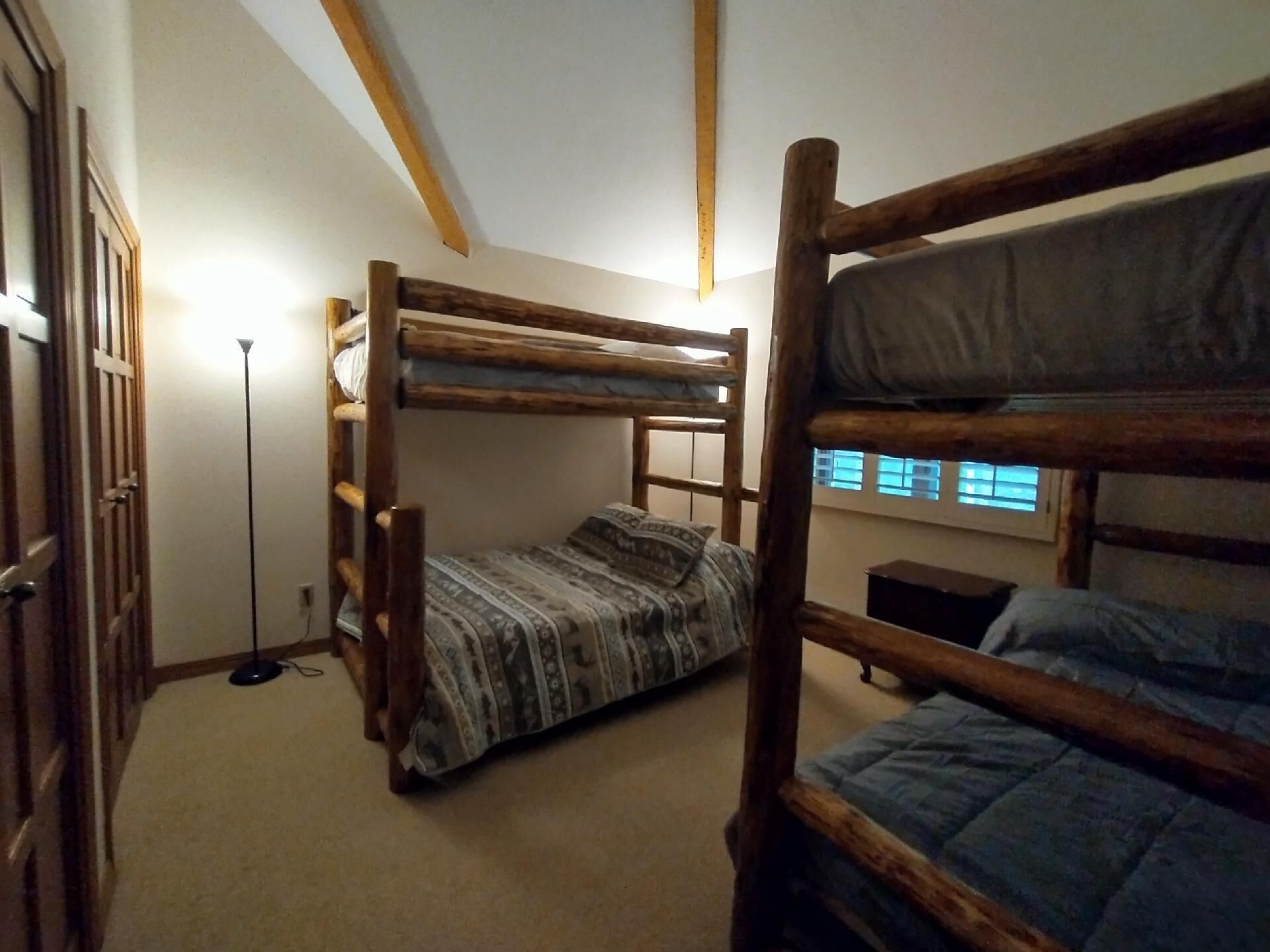 A bunk bed room with a wooden ladder, a patterned bedspread, and a floor lamp.