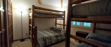 A bunk bed room with a wooden ladder, a patterned bedspread, and a floor lamp.