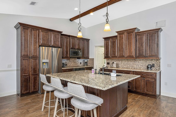 A kitchen with wooden cabinets, a stainless steel refrigerator, granite countertops, and bar stools.