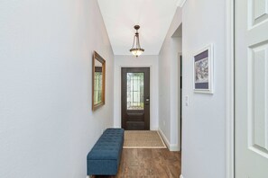 A hallway with a bench, a door with a window, and a hanging light fixture.