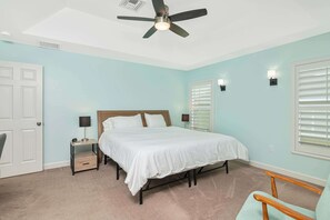 A bedroom with a bed, a nightstand, a ceiling fan, a window with blinds, and a door. - Florida Vacation home with Pool- Near Naples (Bonita Springs)