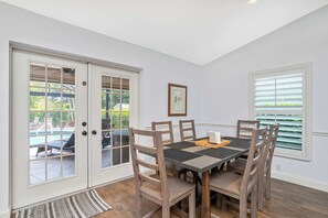 A dining area with a table and chairs, a door with glass panels, and a window with blinds. - Florida Vacation home with Pool- Near Naples (Bonita Springs)