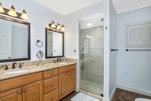 Une salle de bain avec deux lavabos, des meubles en bois, un grand miroir et une cabine de douche en verre.