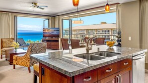 Una cucina moderna con una grande isola, un'area pranzo con vista sull'oceano e un soggiorno con TV e posti a sedere comodi.