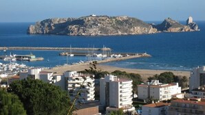 En kystby med en klippeø i baggrunden, en lysthavn med både og bygninger med balkoner med udsigt over havet.