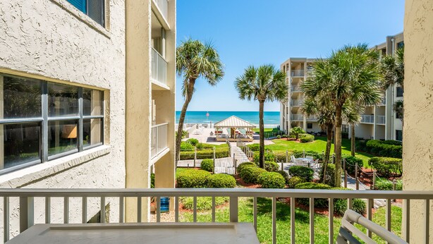 Un balcon avec vue sur une plage, des palmiers et une piscine.