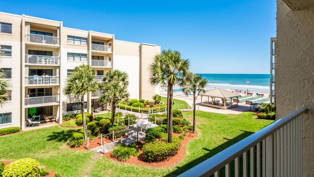 A multi-story hotel with balconies, a landscaped courtyard with palm trees, and a view of the beach. - Castle Reef 326 clean, bright and sure to please! (New Smyrna Beach)