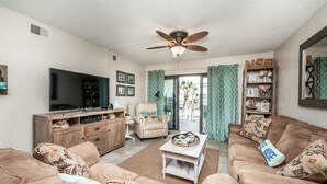 A living room with a TV, a ceiling fan, a sofa, a coffee table, and a bookshelf. - Castle Reef 326 clean, bright and sure to please! (New Smyrna Beach)