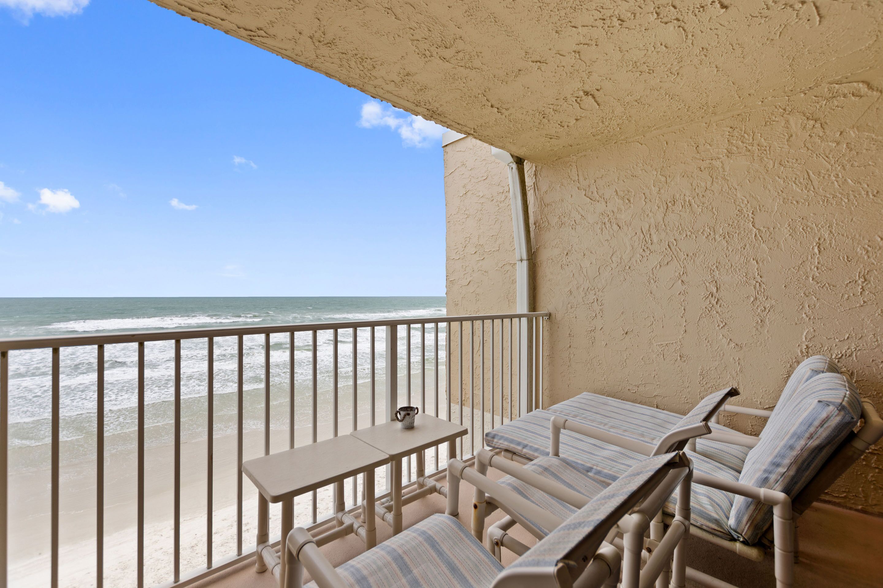 Un balcon avec vue sur la plage, deux chaises longues et une petite table.
