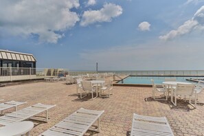 A rooftop pool area with lounge chairs and tables, a pool, and a view of the ocean. - Castle Reef 219 Stay by the Sea (New Smyrna Beach)