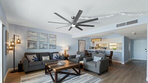 Ein modernes Wohnzimmer mit Deckenventilator, zwei Sofas, einem Couchtisch und einer Küche im Hintergrund.