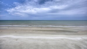 Une plage avec un large rivage sablonneux et une mer calme sous un ciel partiellement nuageux.