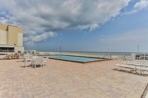 A rooftop pool area with a clear view of the sea, surrounded by lounge chairs and a tiled deck. - Castle Reef 533 stunning direct ocean front view! (New Smyrna Beach)