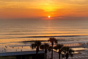 A sunset over the ocean with a boardwalk and palm trees in the foreground. - Castle Reef 511 Beachfront & Sunsets! (New Smyrna Beach)