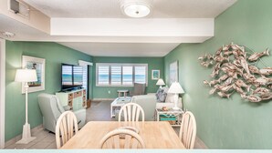 A living room with a TV, seating, and a dining area. - Castle Reef 132  Just Off the Sand (New Smyrna Beach)