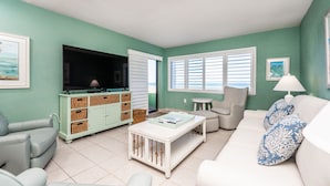 A living room with a television, sofa, armchair, and a coffee table. - Castle Reef 132  Just Off the Sand (New Smyrna Beach)