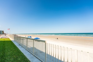 Une plage avec une clôture blanche, une zone herbeuse et un drapeau.
