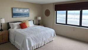 A bedroom with a bed, a painting, a window with a view of the ocean, a lamp, and a wall clock. - Castle Reef - 333 stunning direct ocean front condo on the no drive part of the beach! (New Smyrna Beach)